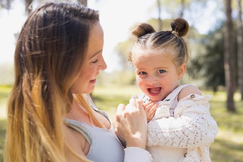 A pregnant woman lovingly embraces her young daughter, sharing a joyful moment outdoors amidst a