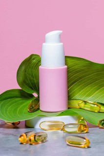 Elegant pink skincare dispenser with a white pump nozzle, framed by a lush green leaf and