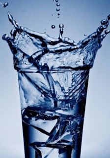 An ice cube cube falls into a glass of cool water, sparkling refreshment in blue duplex toning