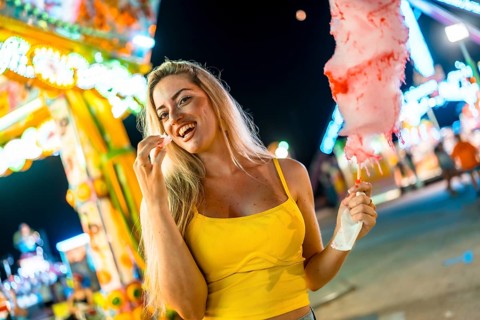 Sensual blonde woman enjoying cotton candy at fair at night