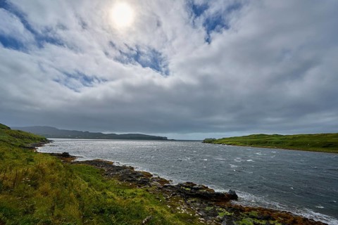 Cloudy sky over an estuary, sun shining through, grassy and rocky coast, Isle of Skye, Scotland,