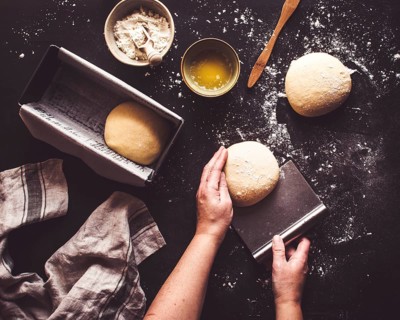 Hands gently shape dough on a floured surface, preparing it for baking. Fresh dough, flour, and a