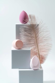 A modern composition featuring cosmetic sponges in pink hues on geometric white blocks, accented