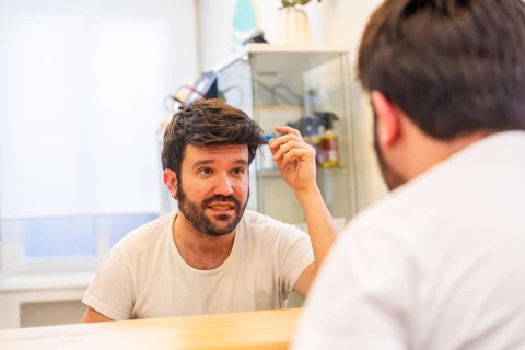 Happy bald man with a new capillary prosthesis looking into hair salon mirror