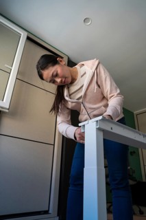 A young Asian woman is focused on assembling a white desk in her home, engaged in a DIY furniture