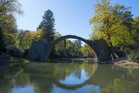 Stone bridge over quiet river with trees reflected in water on a sunny day, Rakotz Bridge, Devil's
