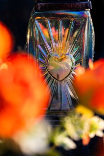 A close-up shot of a decorative glass grave lantern with a heart ornament, placed on a tombstone
