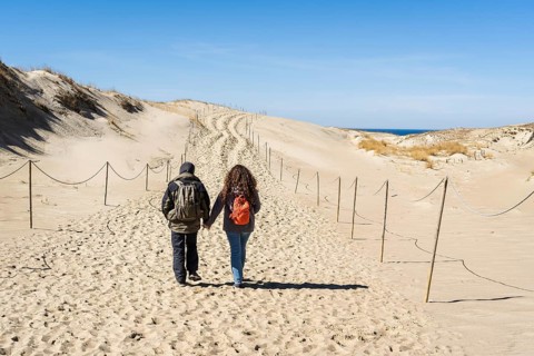 A couple of backpackers walk along a hiking trail in sand dunes on the Curonian Spit near the