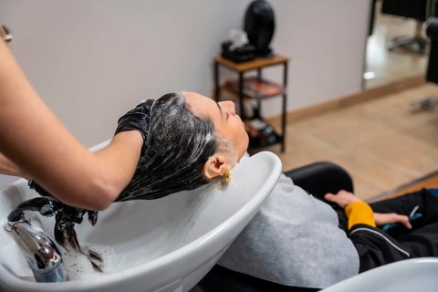 Stylist in black gloves shampooing and massaging a client's dark hair at a salon basin, creating