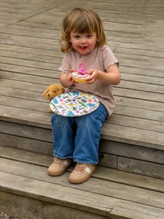 Little Caucasian girl, 3 years old, sitting on a wooden deck and eating a cake in Ystad, Skåne