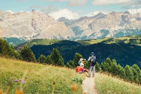 Middle-aged Asian group hikers hike trekking sunny italian Dolomites mountain trail.Alpine meadow