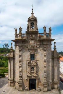 Baroque church with imposing bell tower and decorative sculptures against a cloudy sky, Iglesia de
