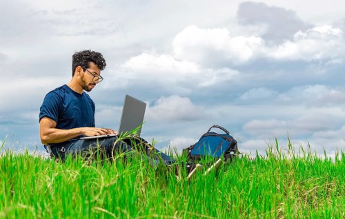 Freelancer man sitting with laptop and backpack in the field. Man sitting in the green field