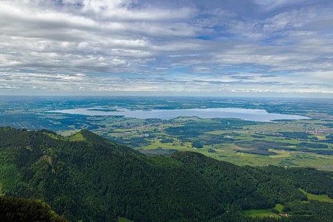 Wide landscape with the Chiemsee in the background, surrounded by green hills and mountains under a