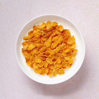 Top view of a white bowl full of crunchy golden cornflakes, isolated on a light textured background