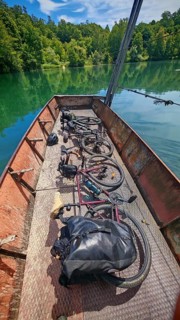 Two bikes on an old crank ferry across the Mreznica river in a quiet, green natural landscape,
