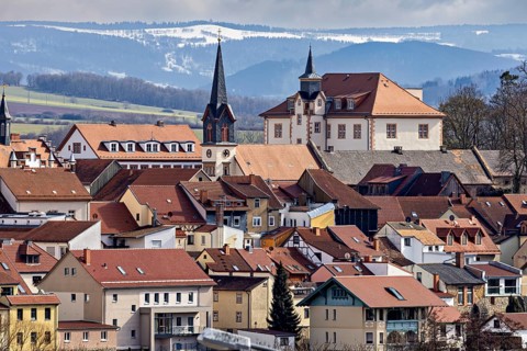 View of church towers and roofs in front of a mountainous landscape and a cloudy sky, the skyline