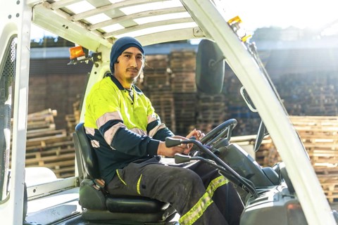 Rays of the sun illuminating a latin man worker driving forklift in a recycling plant