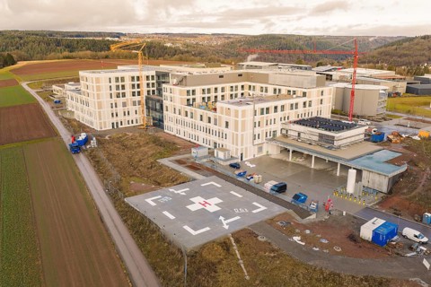 Building and helipad with construction site next to cranes in rural surroundings, shortly in front