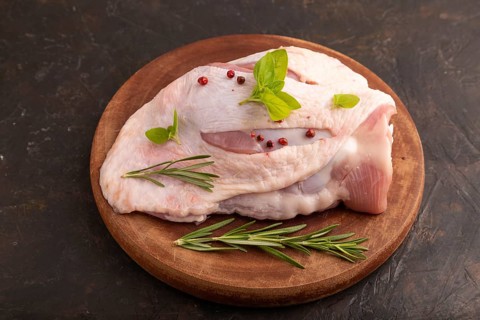 Raw Turkey Thigh with spices and rosemary on cutting board on black concrete background. side view,