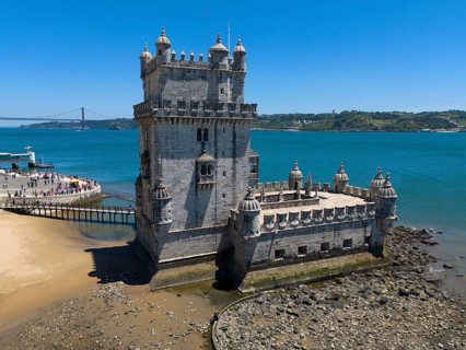 Historic tower on the shore with stones in the foreground and blue sea in the background, aerial