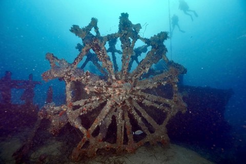 Divers approach a large dilapidated paddle wheel of a shipwreck, dive site Wreck Ville de Grasse,