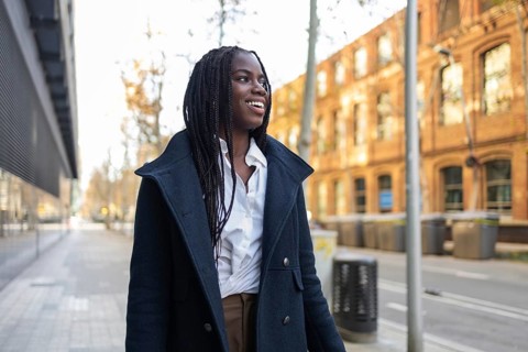 An African American businesswoman with braids, wearing a formal coat over business attire, enjoys