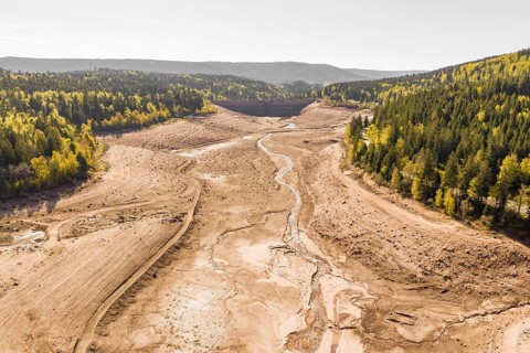 Dry riverbed surrounded by wooded slopes in autumn colors, emptied Schwarzenbach dam, Forbach,
