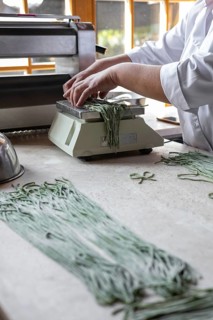 Woman preparing handmade pasta. Woman's hands working with dough to make pasta. Chef making green