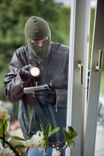 A burglar with flashlight and pistol, breaking into a family home, studio shot, Austria