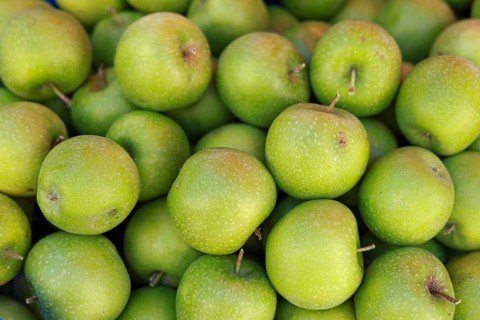 A pile of fresh green apples, showcasing their glossy skin and vibrant hue, symbolizing health and