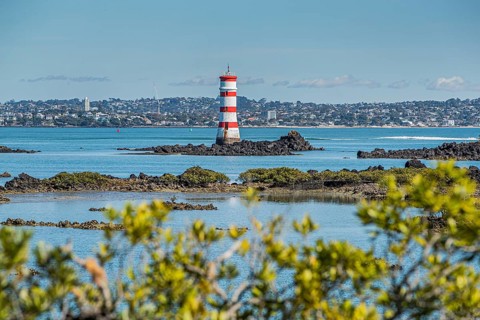 The red and white striped Rangitoto Beacon, built in 1882 off McKenzie Bay, stands beyond weathered