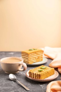 Homemade honey cake with milk cream and mint with cup of coffee on a black and orange background