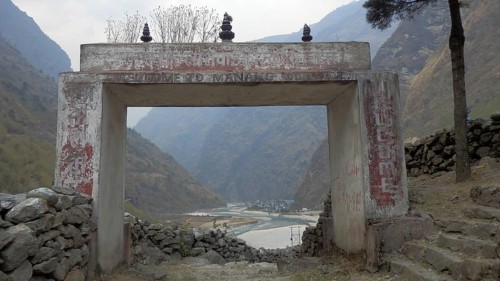 A stone gate with the inscription Welcome to Manang, overlooking a valley and a river, trekking at