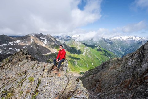 Mountaineer sitting on a rock, on a steep rocky ridge, on the summit of the Lasörling, view of the