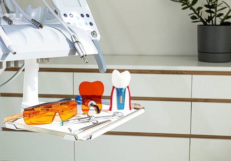 On the tray are various dental instruments, a model dental implant and bright orange safety