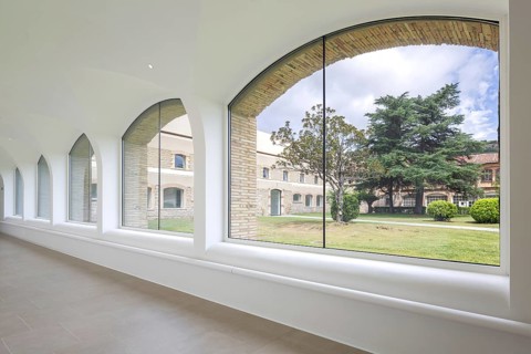 View os hospital through elegant arched windows in a bright corridor, overlooking a lush garden and