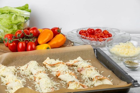 Pizza sticks on a tray sprinkled with grated cheese, surrounded by fresh ingredients, pizza