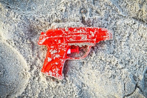 Red water pistol in the sand +++ editorial use only