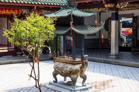 Smoking joss sticks rise from a dragon carved Bronze incense burner beneath a pagoda roof in the