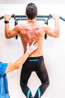 Back of a shirtless patient with a physical therapist in a dominated one. Physiotherapy with
