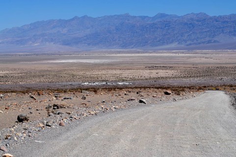 Gravel road leads into the dry, wide plain with mountains in the background, Death Valley National