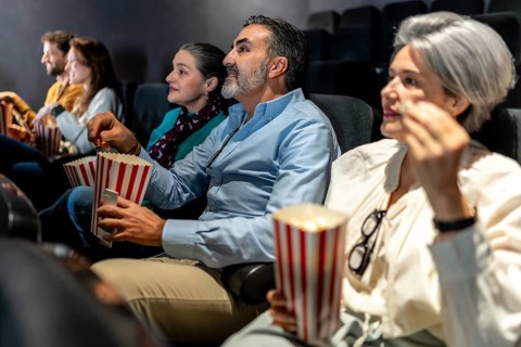 Group of friends sharing laughter and enjoying popcorn while watching an exciting film screening in