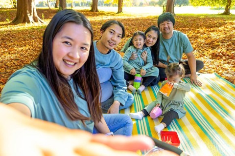 Happy Asian family having a joyful picnic outdoors, sitting on a blanket surrounded by autumn