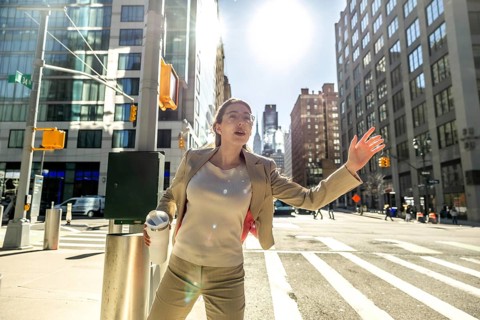 Busy businesswoman with a travel mug actively hailing a taxi on a sunny day in manhattan,
