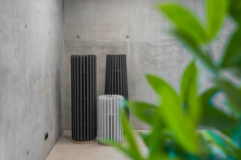 Three modern abstract columns in front of a concrete wall with plants in the foreground, Boarding