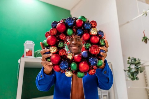 Close up young happy fun african man 20s in sweater look through Advent wreath on green background.
