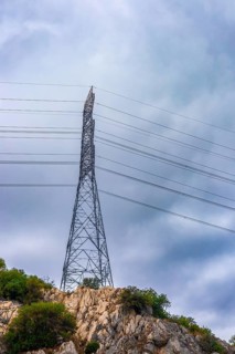 A tall electricity transmission tower stands on a rocky hill. Power lines stretch across the sky