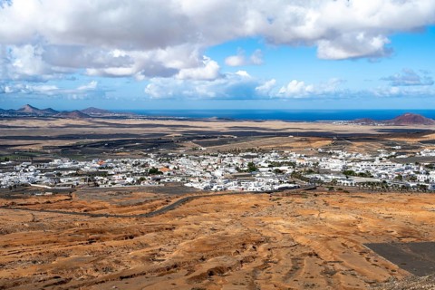 View of town, white houses of Teguise with church tower in dry volcanic landscape, Lanzarote,