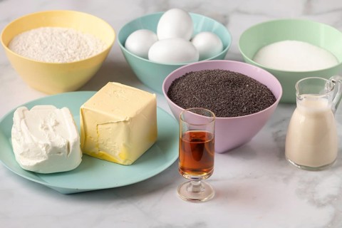 Baking ingredients with a piece of butter, eggs, quark and poppy seeds in colorful bowls